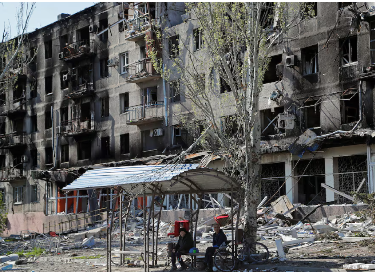 Locals sit on a bench near an apartment building damaged during the Ukraine-Russia conflict in the southern port city of Mariupol, Ukraine. April 28, 2022. Reuters/Alexander Ermochenko